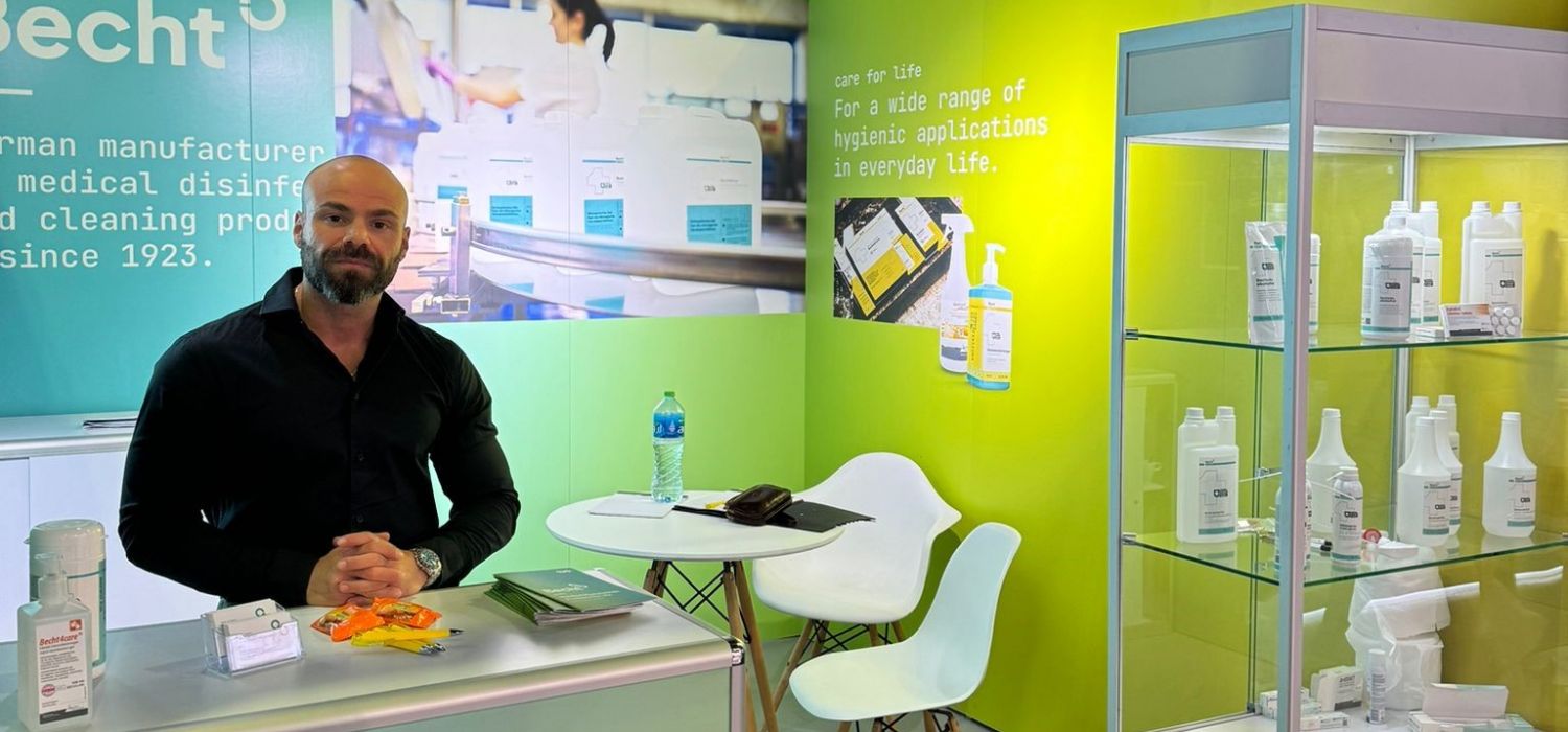 Becht-Messestand Arab Health 2025 Becht-Messestand mit Produkten für medizinische Desinfektion und Reinigung. Mitarbeiter am Empfangstisch mit Broschüren und Desinfektionsmittel.