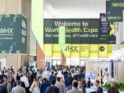 Besucher in der modernen Messehalle der World Health Expo WHX. Großes Veranstaltungs-Banner „The new home of Healthcare“ und Werbe-Displays für die Gesundheitsmesse.