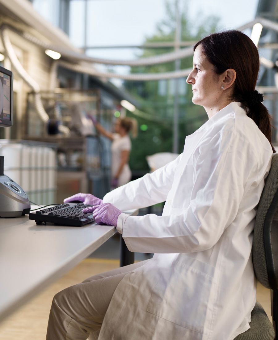 Laborantin der Alfred Becht GmbH führt Qualitätskontrollen an einem Analysegerät durch und wertet Messergebnisse am Computer aus.