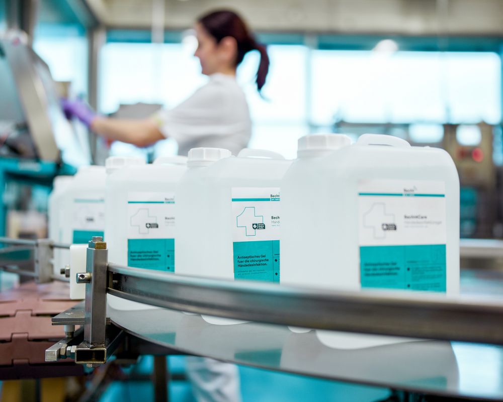 Mitarbeiterin der Alfred Becht GmbH arbeitet an einer Abfüllanlage, während Kanister mit Desinfektionsmitteln auf einem Förderband vorbeilaufen.