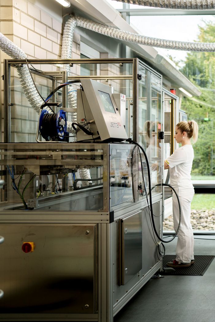 An employee of Alfred Becht GmbH stands at a window with her laptop and documents in her arms and smiles.