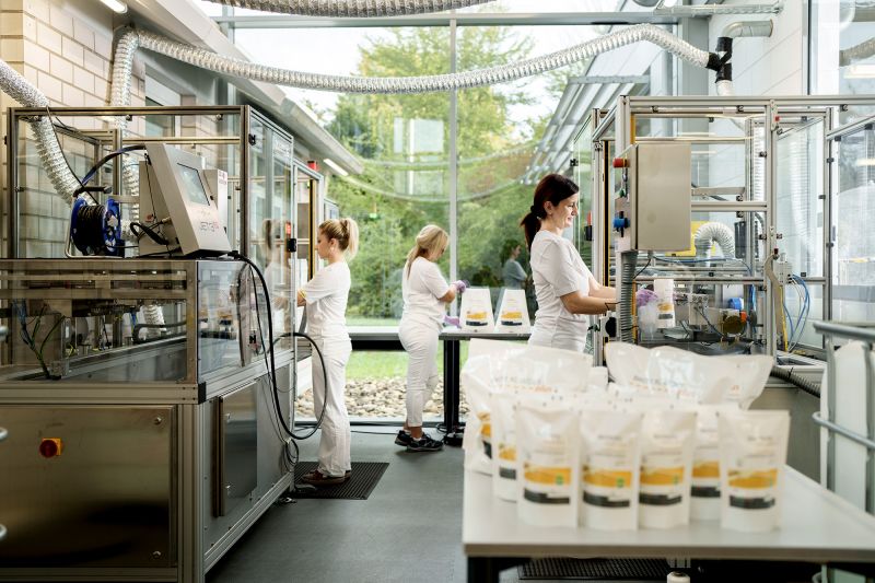 Mitarbeiterinnen der Alfred Becht GmbH arbeiten in einer modernen, lichtdurchfluteten Produktionshalle an Anlagen zur Herstellung von Medizinprodukten.