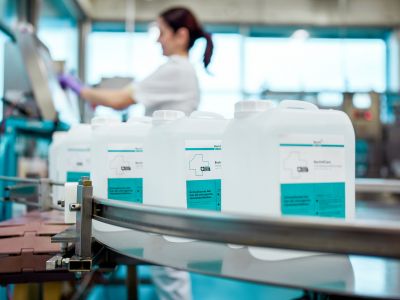 Mitarbeiterin der Alfred Becht GmbH arbeitet an einer Abfüllanlage, während Kanister mit Desinfektionsmitteln auf einem Förderband vorbeilaufen.