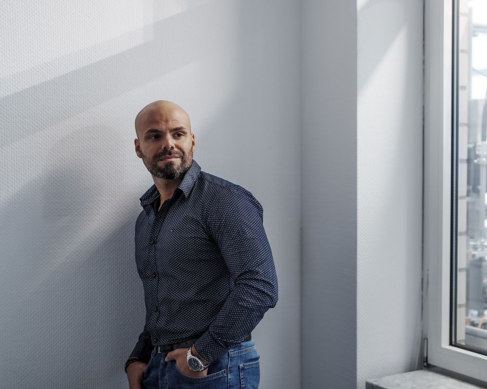 An employee of Alfred Becht GmbH stands casually by a window, looking outside.
