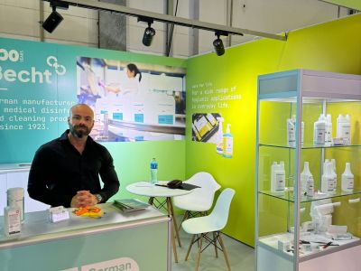 Becht-Messestand mit Produkten für medizinische Desinfektion und Reinigung. Mitarbeiter am Empfangstisch mit Broschüren und Desinfektionsmittel.