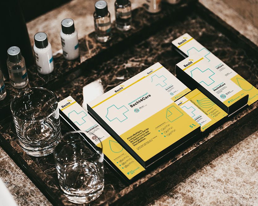 Becht4Care products in yellow and white packaging on a marble washbasin, surrounded by small bottles and jars.