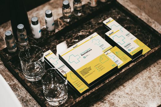 Becht4Care products in yellow and white packaging on a marble washbasin, surrounded by small bottles and jars.