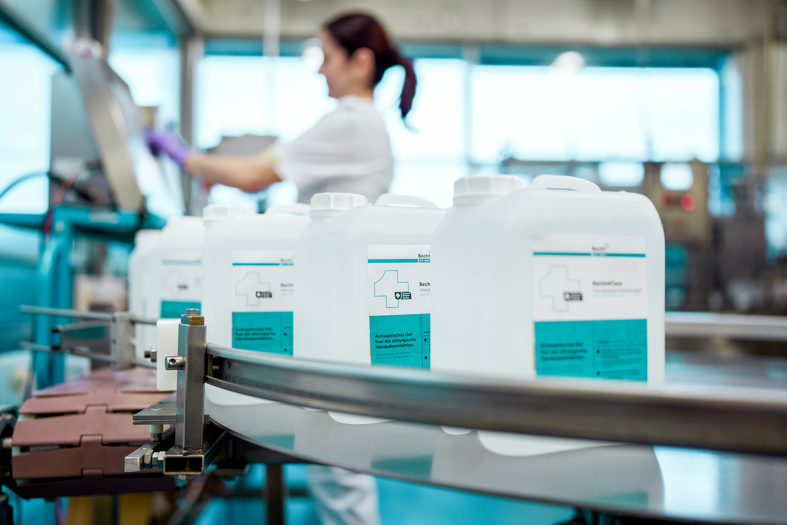 Mitarbeiterin der Alfred Becht GmbH arbeitet an einer Abfüllanlage, während Kanister mit Desinfektionsmitteln auf einem Förderband vorbeilaufen.