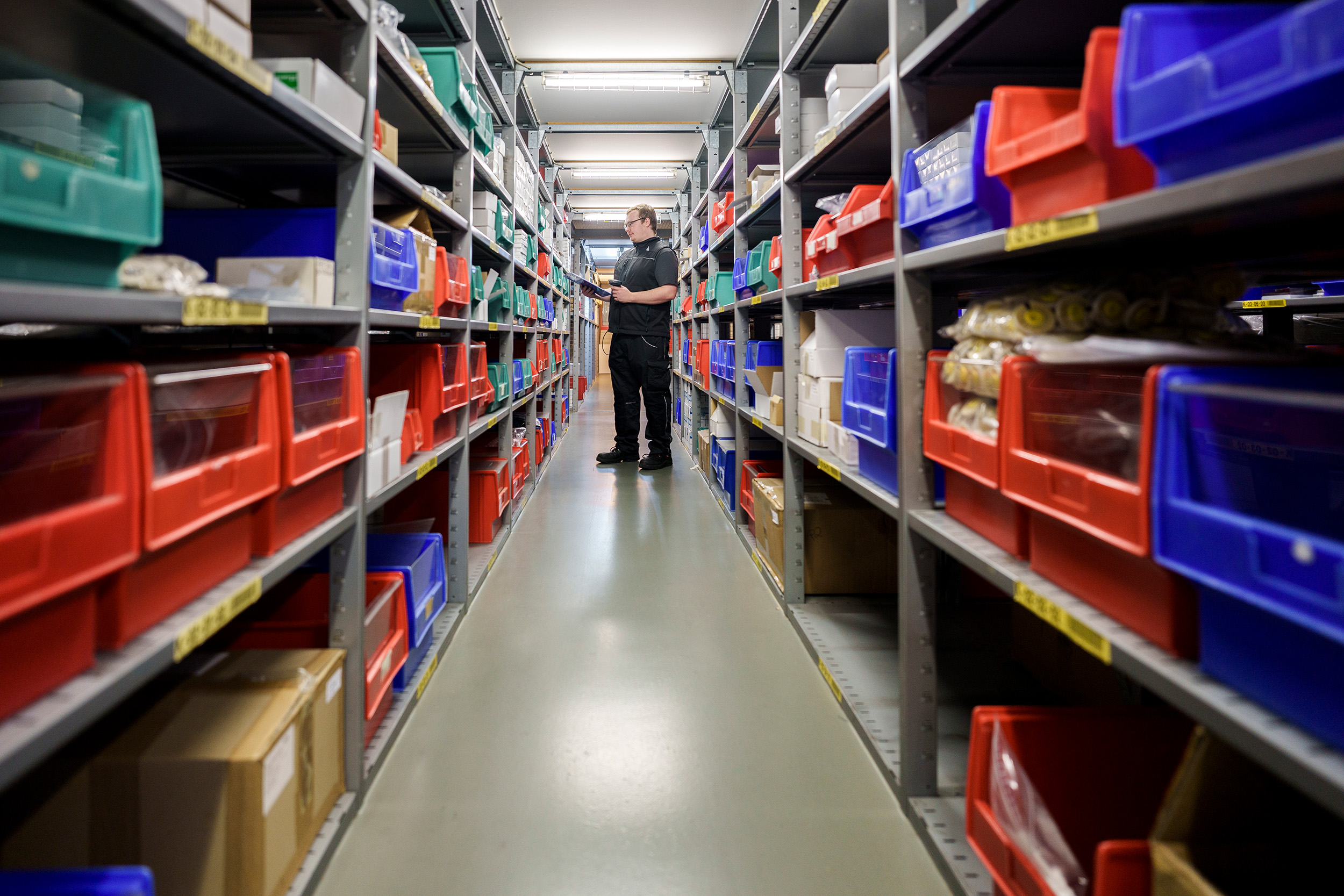 Employee at Alfred Becht GmbH checking inventory in a well-organized warehouse with colored plastic bins and medical components.